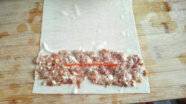 将干豆腐铺到菜板上面，抹上适量肉馅，放一根胡萝卜丝，从下往上卷好